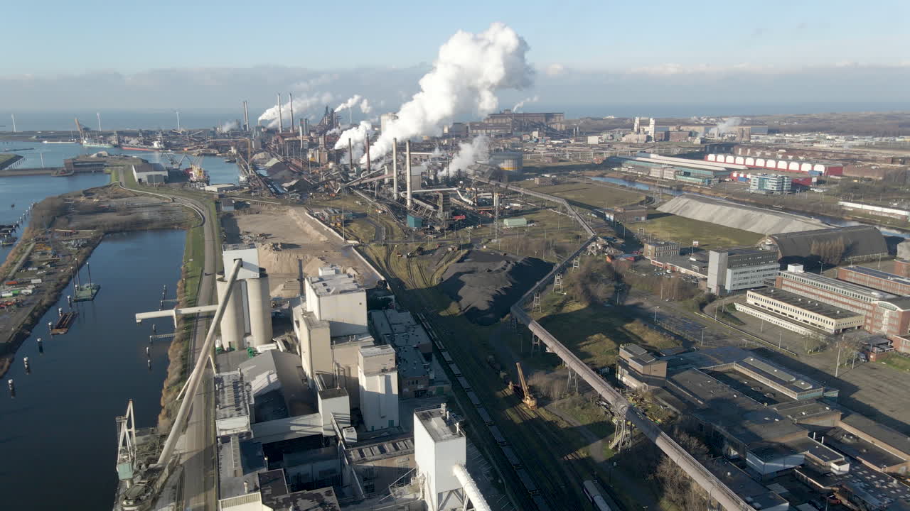 Aerial of distant large steel mill with smoking chimneys