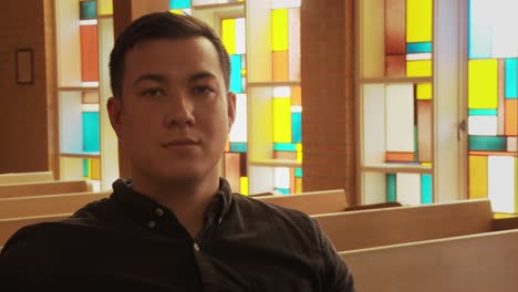 close up of a young ethnic man staring into the camera with a solemn face while sitting inside a church sanctuary