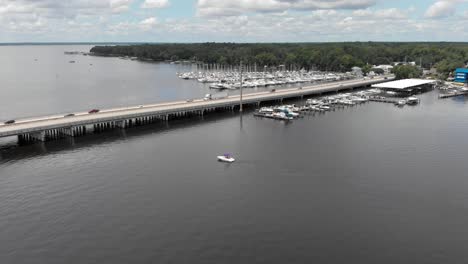 Zoom-out-of-water-boat-marina-with-bridge-boats-in-the-background-trees-in-the-background-white-clouds-blue-sky