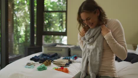 happy caucasian pregnant woman looking on baby clothes while packing suitcase to hospital