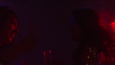 close up of two women in nightclub bar or disco dancing and drinking alcohol with sparkling lights