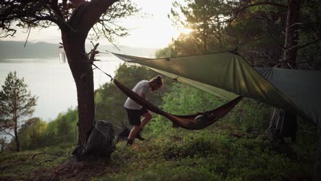 a tourist guy relaxing outdoors lying on a camping hammock hanging on a hillside