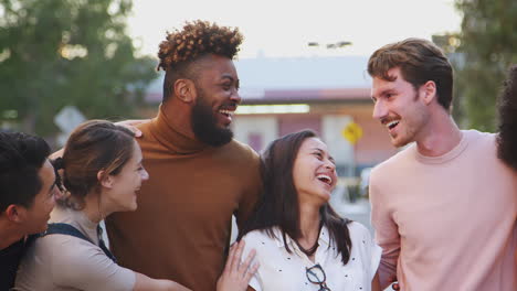 six millennial hipster friends standing in a city street smiling to camera, panning shot