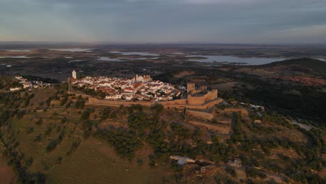 Drohne-Fliegt-über-Das-Dorf-Monsaraz-Mit-Dem-Fluss-Alqueva-Im-Hintergrund-In-Der-Dämmerung,-Portugal