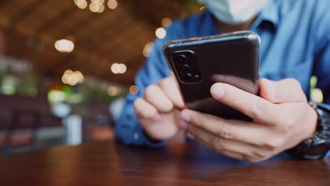 een jonge zakenman met een chirurgisch masker houdt een videoconferentie met klanten via een smartphone die verbonden is met het internet.