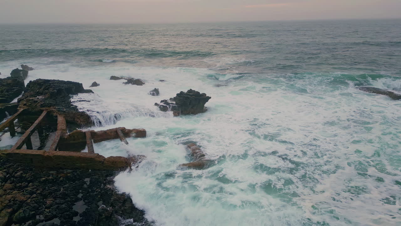 Vista panoramica di onde oceaniche sotto un cielo nuvoloso. Scala di legno abbandonata giacente sulle rocce