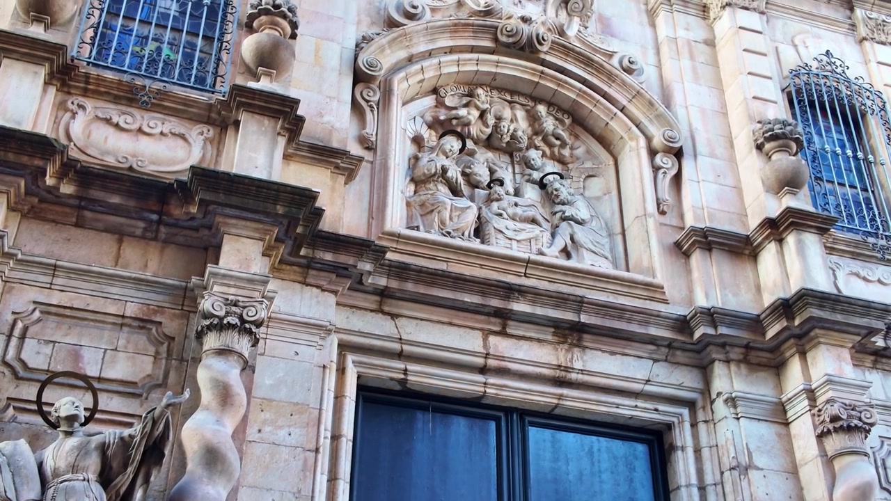 La Chiesa di Betlem su La Rambla a Barcellona, Catalogna, Spagna, mostra una facciata barocca con colonne salomoniche, rilievi in pietra intagliati e sculture religiose, con la telecamera che panoramica sui dettagli architettonici.