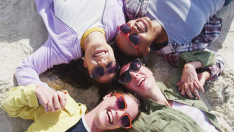 happy group of diverse female friends having fun, holding hands and smiling at the beach