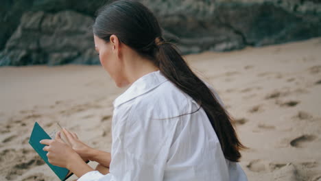 una mujer joven leyendo un libro sentada en una playa de arena de cerca. una chica relajándose en la orilla del mar