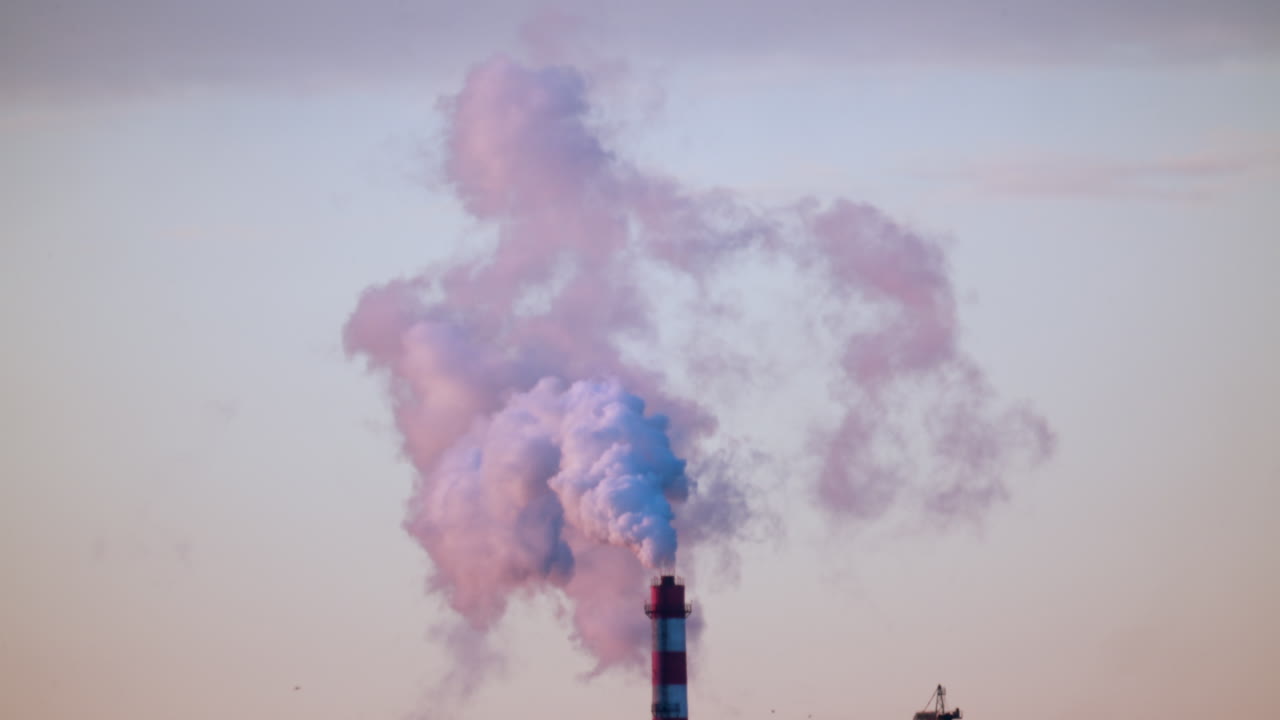 Ciminiera industriale che rilascia fumo denso nel cielo sopra un cantiere edile cittadino.