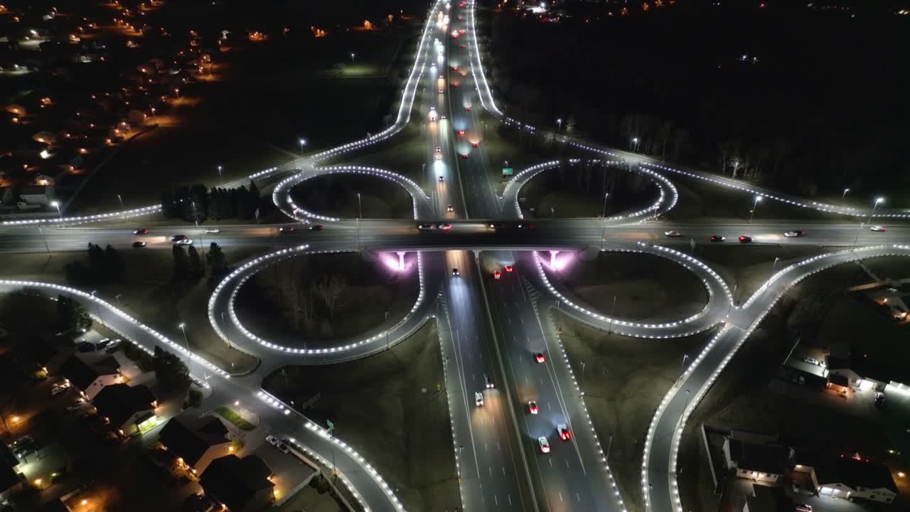 Opening topdown camera filming purple cloverleaf interchange at night, vehicles moving for commute
