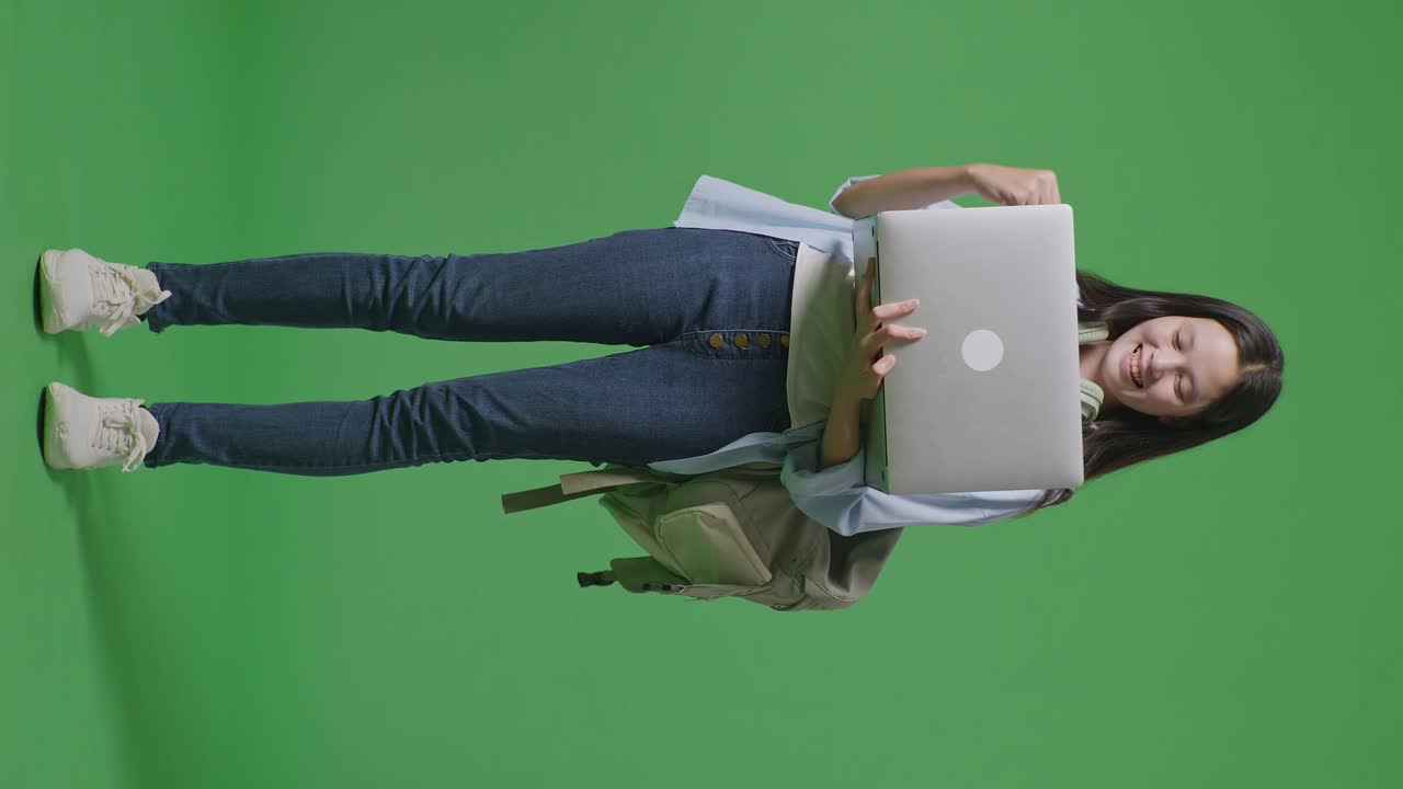 cuerpo lleno de estudiante adolescente asiática con una mochila usar portátil y celebrar mientras está de pie en la pantalla verde estudio de fondo