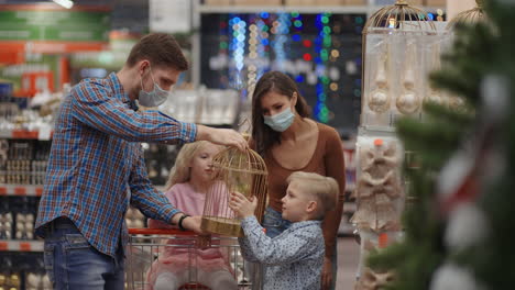 una familia feliz con máscaras médicas en la tienda compra decoraciones de navidad y regalos en cámara lenta. cuatro personas padre hijo hija y madre