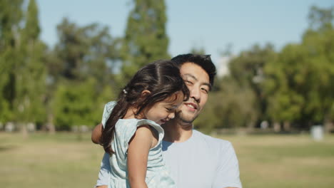 Glücklicher-Asiatischer-Junger-Vater,-Der-Mit-Kleiner-Tochter-In-Den-Armen-Im-Park-Spaziert