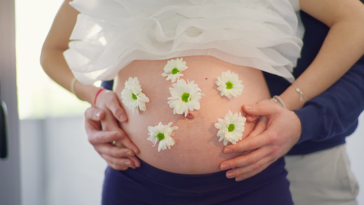 Close Up of Pregnant Woman's Belly with Flowers and Partner's Hands