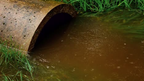 dirty drain water flows rapidly from a concrete pipe, creating a turbulent stream