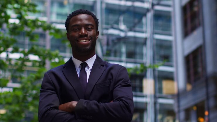 Portrait Of Confident Smiling Young Businessman Wearing Suit Folding Arms Standing Outside Offices In The Financial District Of The City Of London UK 1