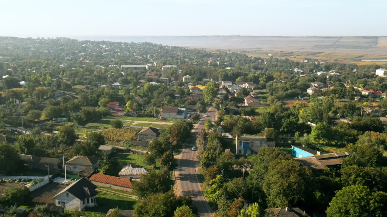 Dronebillede i fugleperspektiv af en landsby i Moldova. Boligbygninger, vej med biler i bevægelse, grønne områder, marker rundt omkring