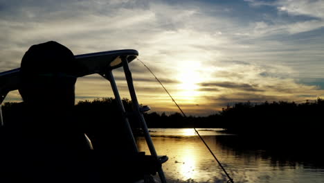 silhouette of man driving fishing boat, sunrise in background, slow motion