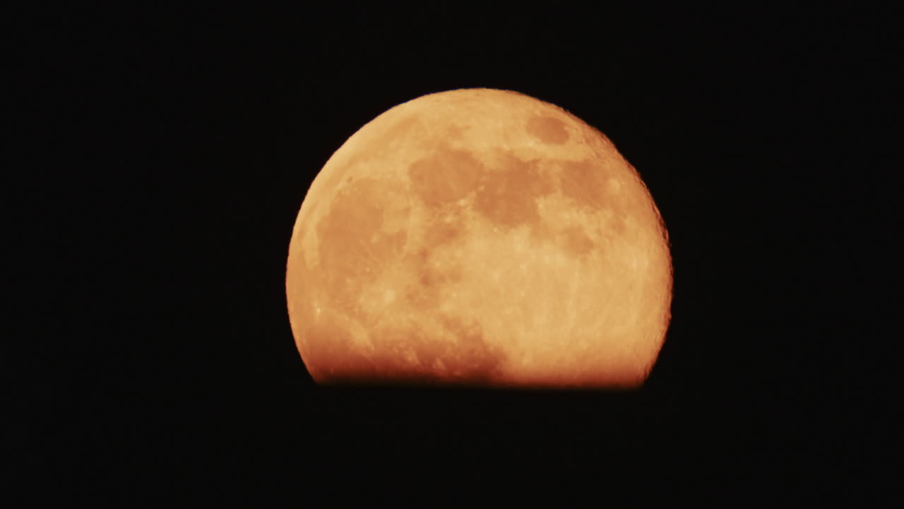 Large full moon rising against a dark night sky with clear details and dramatic atmosphere