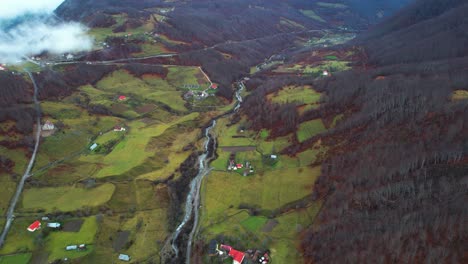 Colorful-countryside-landscape-in-Albanian-Alps,-houses-and-meadows-surrounded-by-Autumn-colors-of-mountains