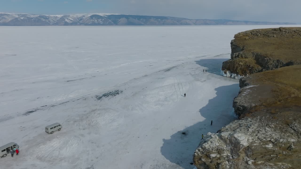 Droneoptagelser af Kap Kharantsy på Olkhon-øen, Irkutsk Oblast, Rusland, der viser stejle kystklipper, enorm frossen Bajkalsø-is og små mennesker, der går nedenfor