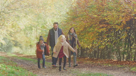 family walking along track in autumn countryside with children running ahead