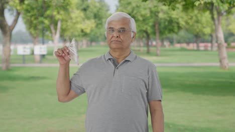 Confident-Indian-old-man-using-money-as-fan-in-park