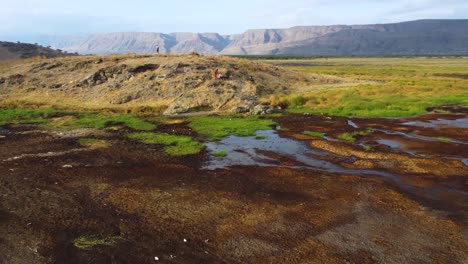 An-impressive-view-of-the-stunning-landscape-of-Lake-Natron-in-Tanzania,-with-people-standing-on-a-hilltop-with-the-amazing-mountains-in-the-background-on-a-clear-blue-day-in-North-Africa