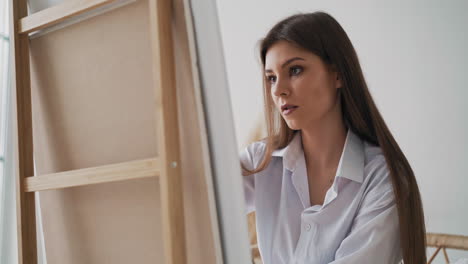 woman in shirt draws painting on white canvas in art studio