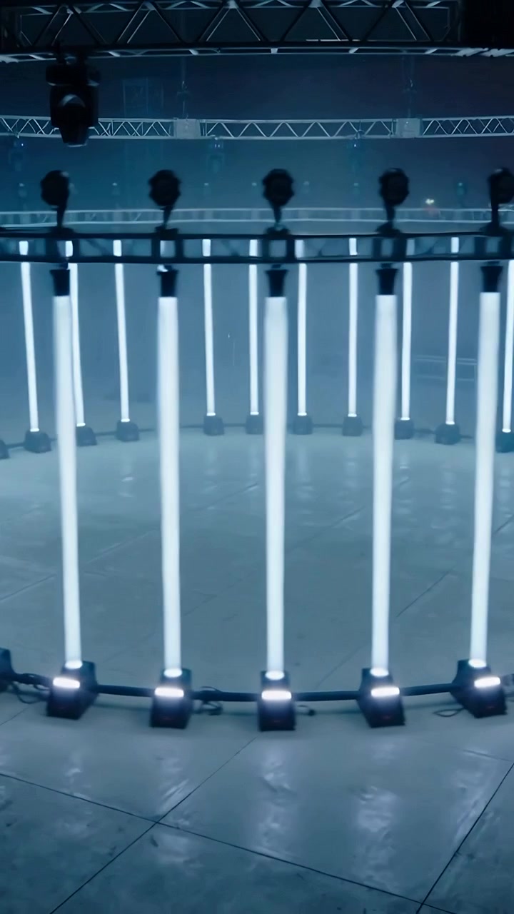 Video verticale: La telecamera si allontana, rivelando un anello LED in uno studio in penombra, con un traliccio per l'allestimento scenico.