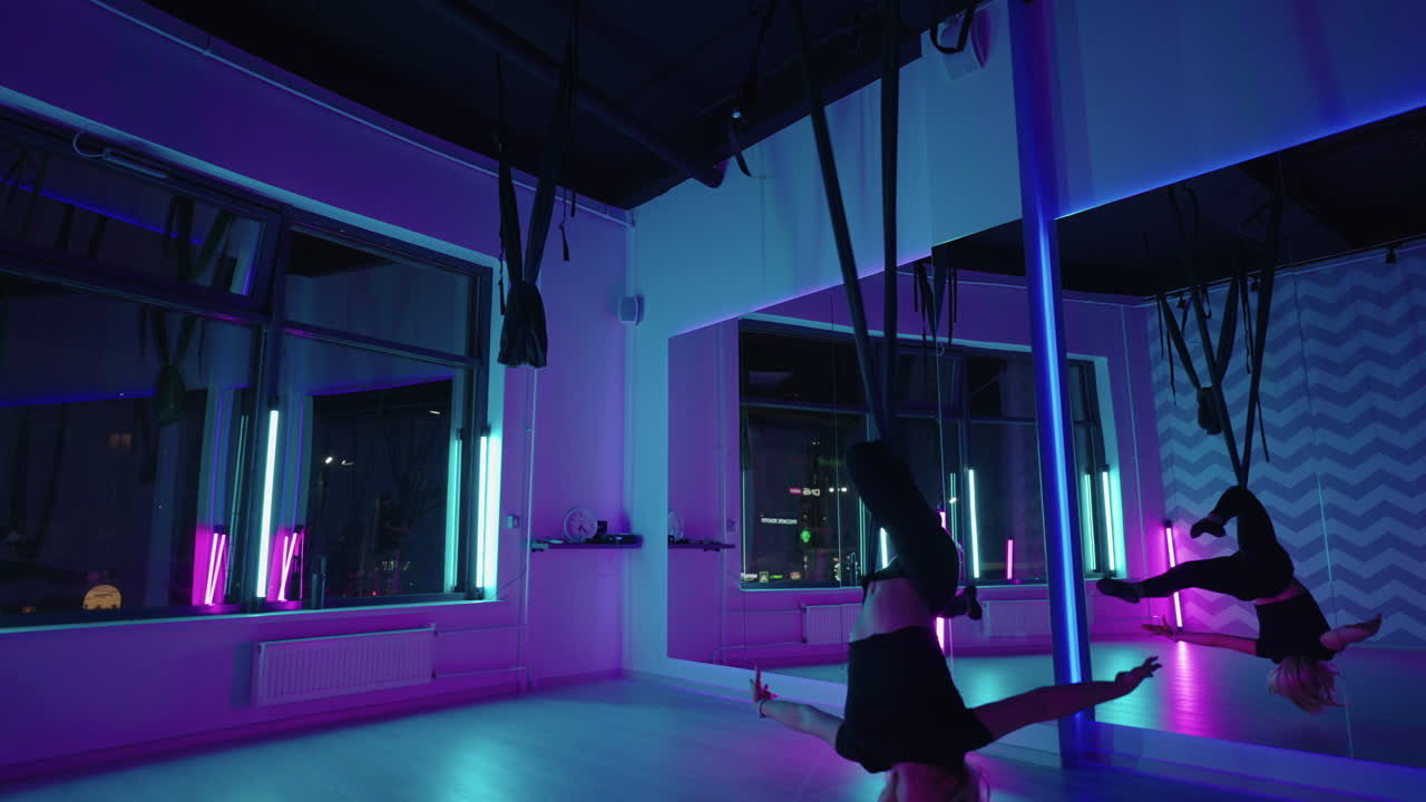 한 여자가 요가를 하고 네온 빛에 매달린 하마크에서 스트레칭을 하고 있습니다. 젊은 예쁜  ⁇ 은 몸의 피트니스 소녀가 체육관에서 플라이 요가를 연습하고 있습니다.