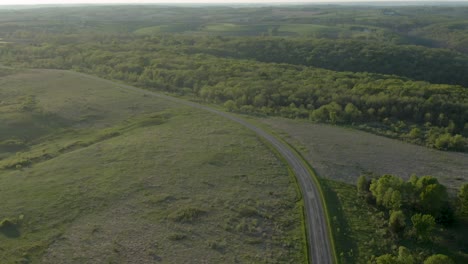 Aerial-shot-of-a-country-road-between-green-meadows-and-a-thick-forest-in-the-mountains-of-Wisconsin,-USA