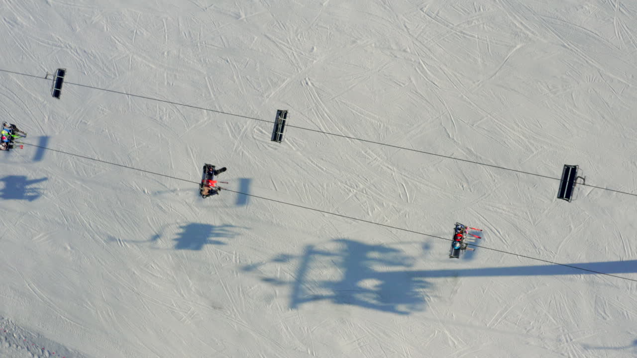 Aerial shot looking directly down on a ski lift carrying skiers over a snowy slope on a sunny day. Drone top down on chair lift