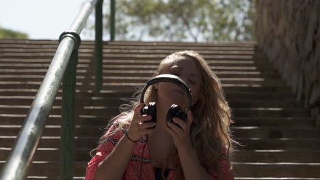 beautiful blonde woman puts on headphones while sitting in park