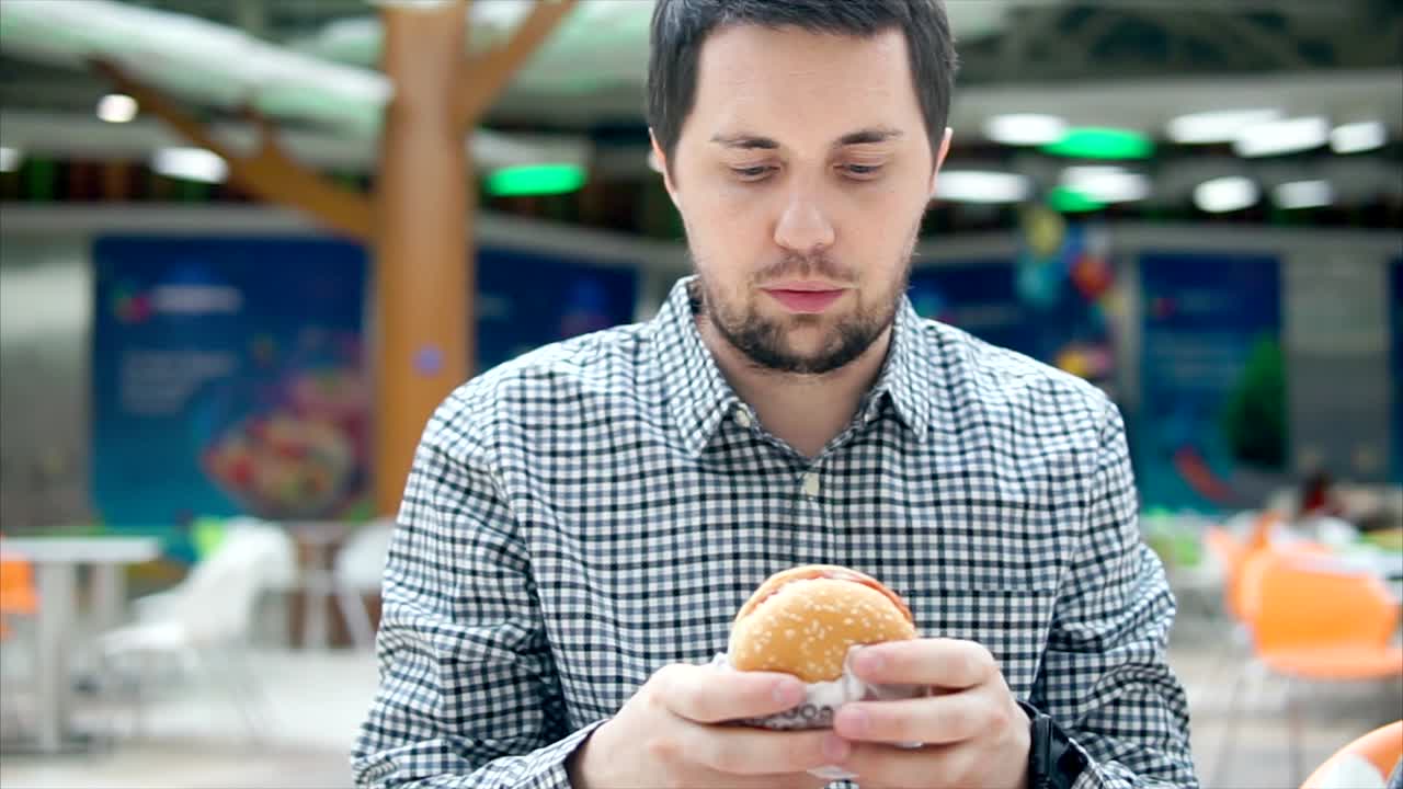 hombre comiendo una hamburguesa en una sala de comidas del centro comercial