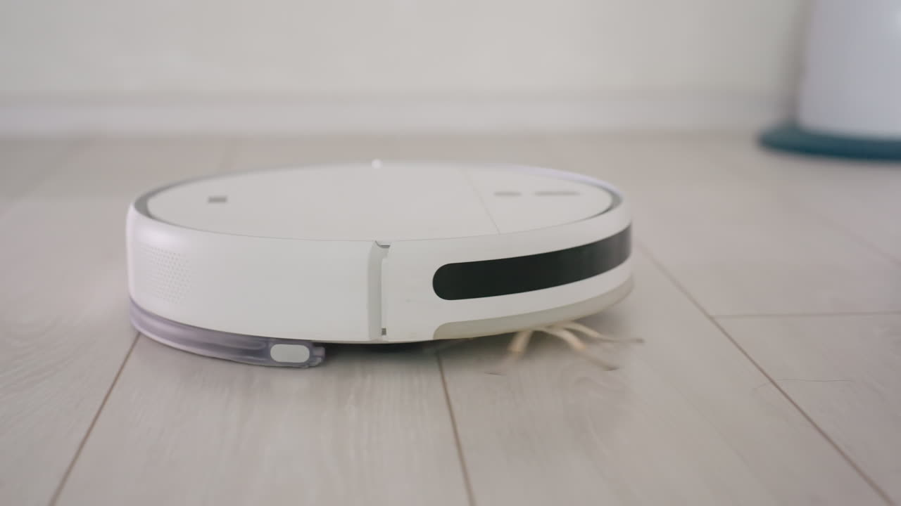 Robot vacuum cleaner glides smoothly across wooden floor during cleaning cycle, showcasing modern smart appliance efficiency and automated home technology for household maintenance