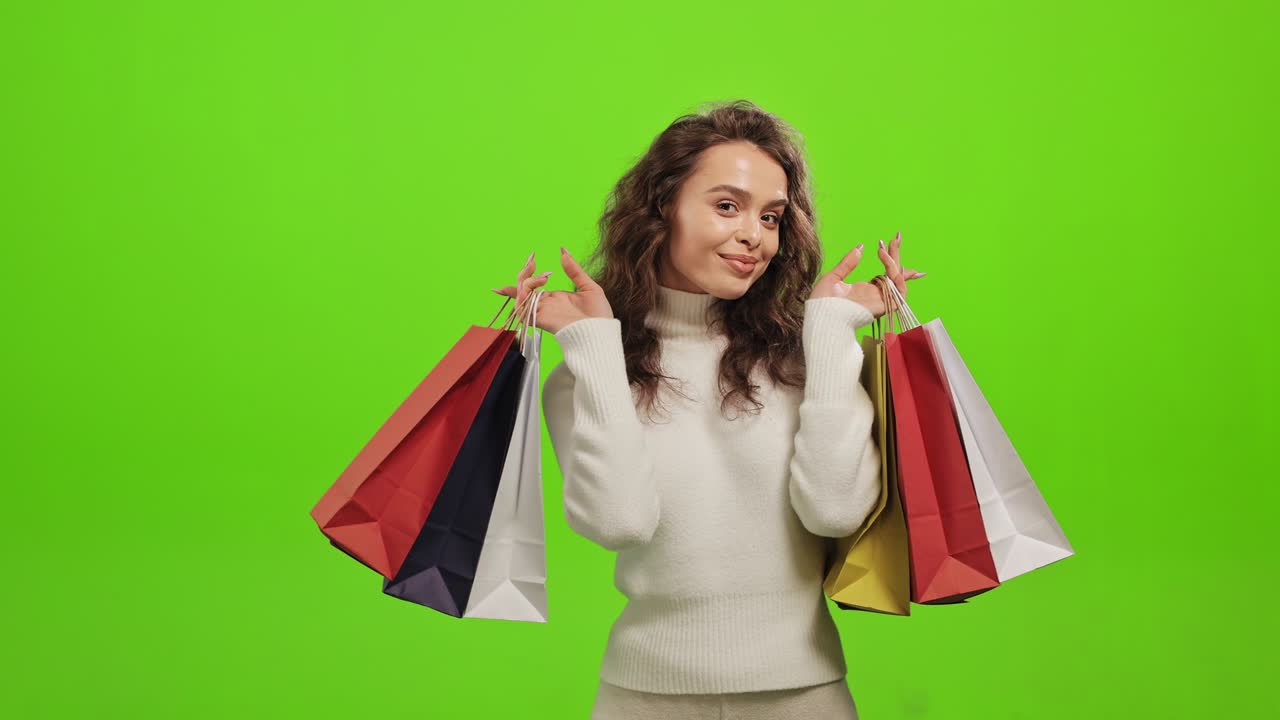 la mujer está mirando a la cámara y sonriendo. está levantando las bolsas de compras. está de pie sobre un fondo verde. pantalla verde. 4k.