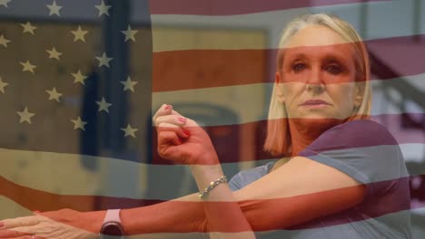 animation of national flag of america over senior caucasian woman doing stretching at gym