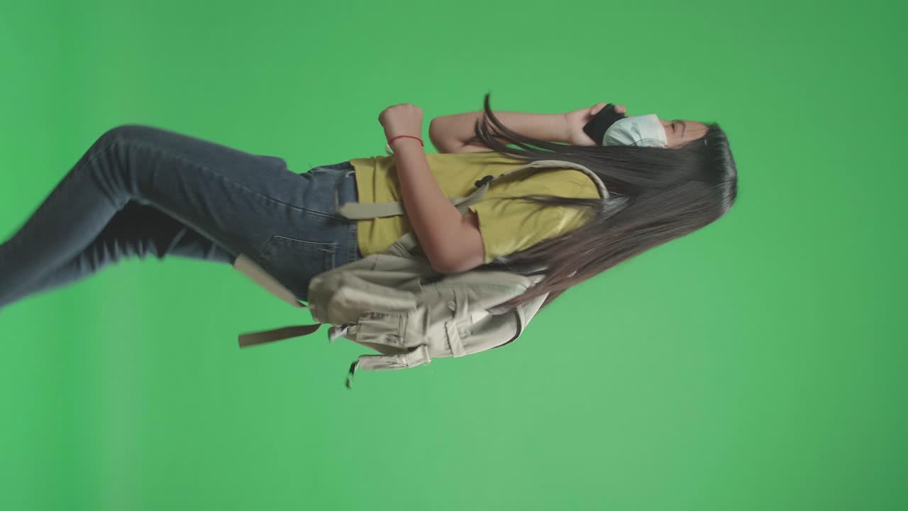 Side View Of Asian Girl Student Wearing A Mask And Talking On Mobile Phone While Running To School On Green Screen Chroma Key