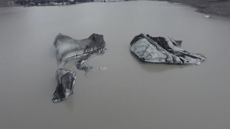 vista aérea sobre bloques de hielo ennegrecidos en la laguna del glaciar solheimajokull - inclinación, disparo de drones