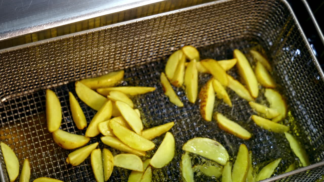Pieces of potato in deep fryer before cooking. Many bubbles appears in hot oil. Process of frying potato in boiled oil.