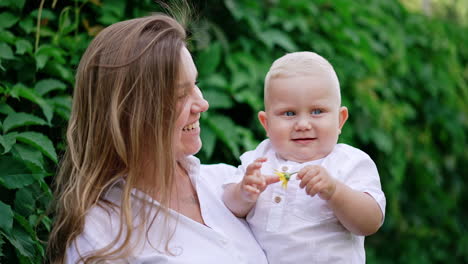 attractive long-haired caucasian woman holding a cute blond baby boy. happy mother with her beloved son holding a flower in hand.