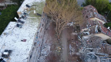top-down drone shot of a devastated neighborhood in tel aviv. a tree lies in the center, surrounded by ruins and destroyed buildings on both sides