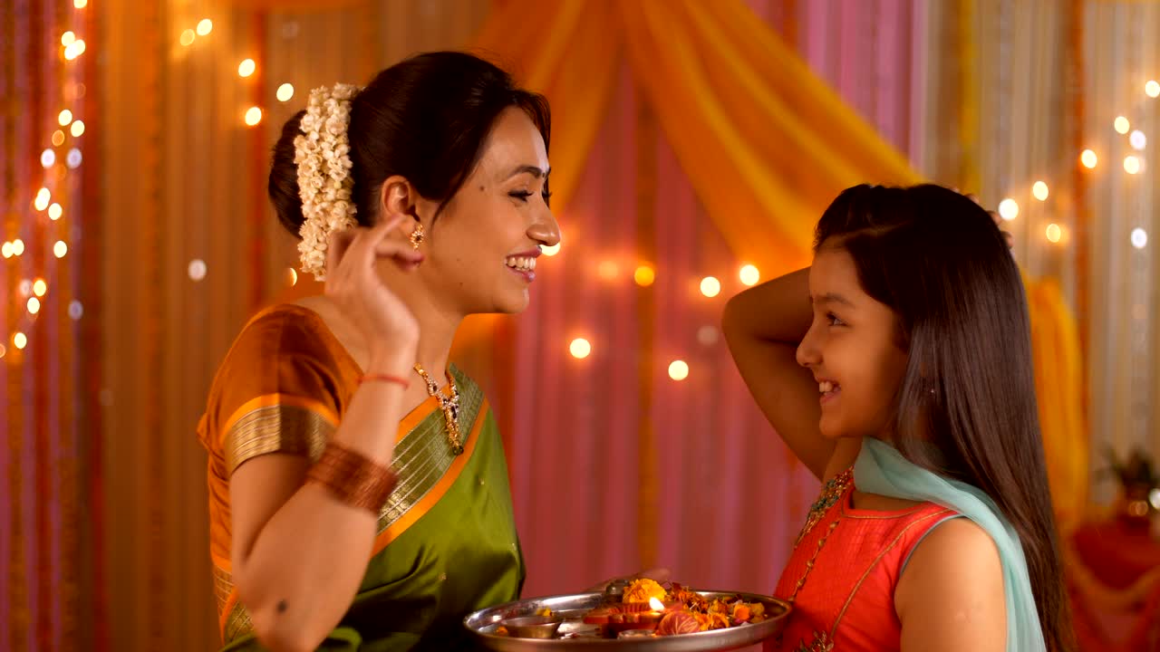 Mother putting tilak on young daughter's forehead - Celebration at home. Festive colorful background