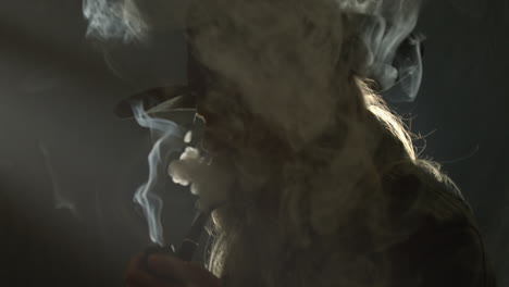 backlit cowboy silhouette surrounded by smoke in dark room smokes pipe