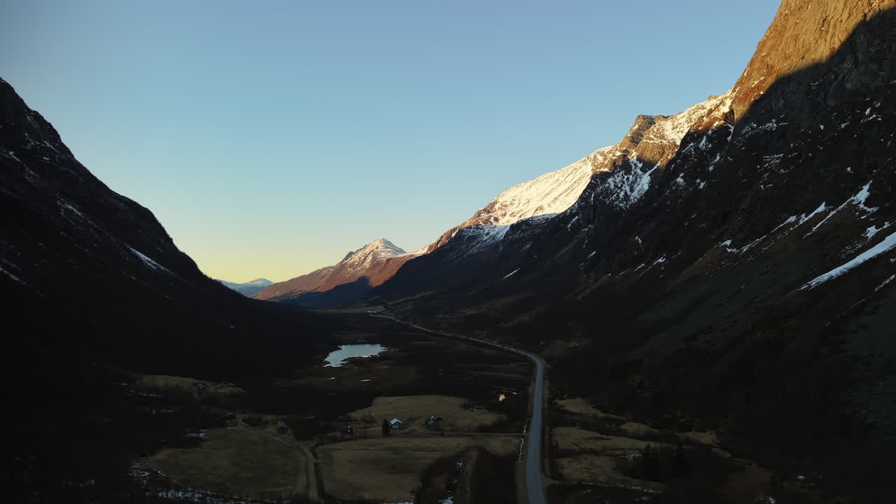 Una strada si snoda attraverso una valle montuosa con cime innevate all'alba. Ideale per documentari di viaggio o sulla natura