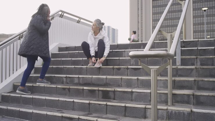 Mature White woman threading pink sneaker laces on stone stairs before run, checking fitness watch