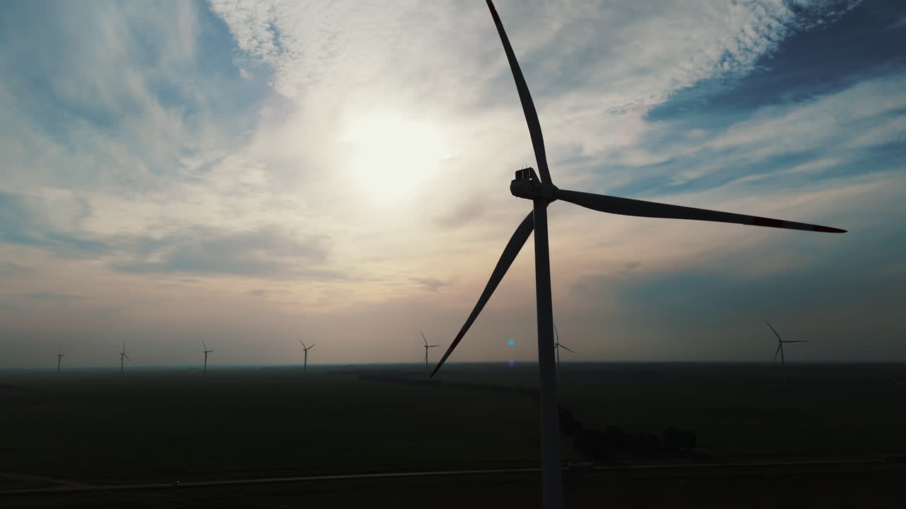 Silhouette of a windmill at sunset, sunrise with cloudy sky, more windmills in the background, blue, truck shot, copy space