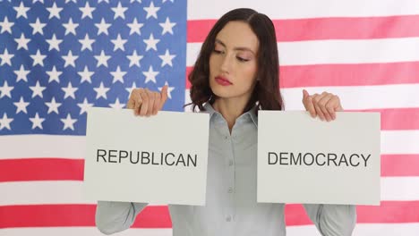 woman holding 'republican' and 'democracy' signs in front of an american flag